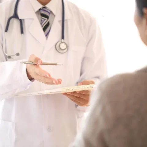 A doctor in a white coat holding a clipboard while talking with a patient