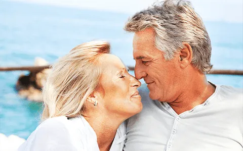 An older couple touching noses by the sea