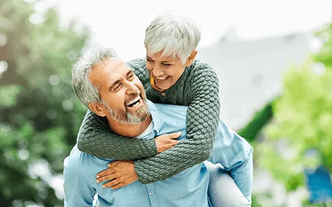 A laughing older man giving his partner a piggyback ride outdoors
