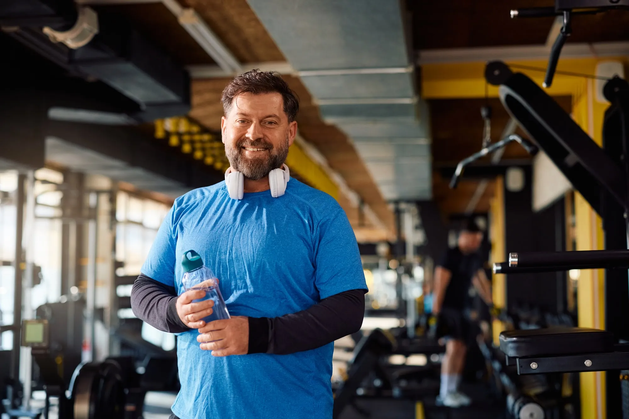 A smiling middle-aged man holding a water bottle at the gym
